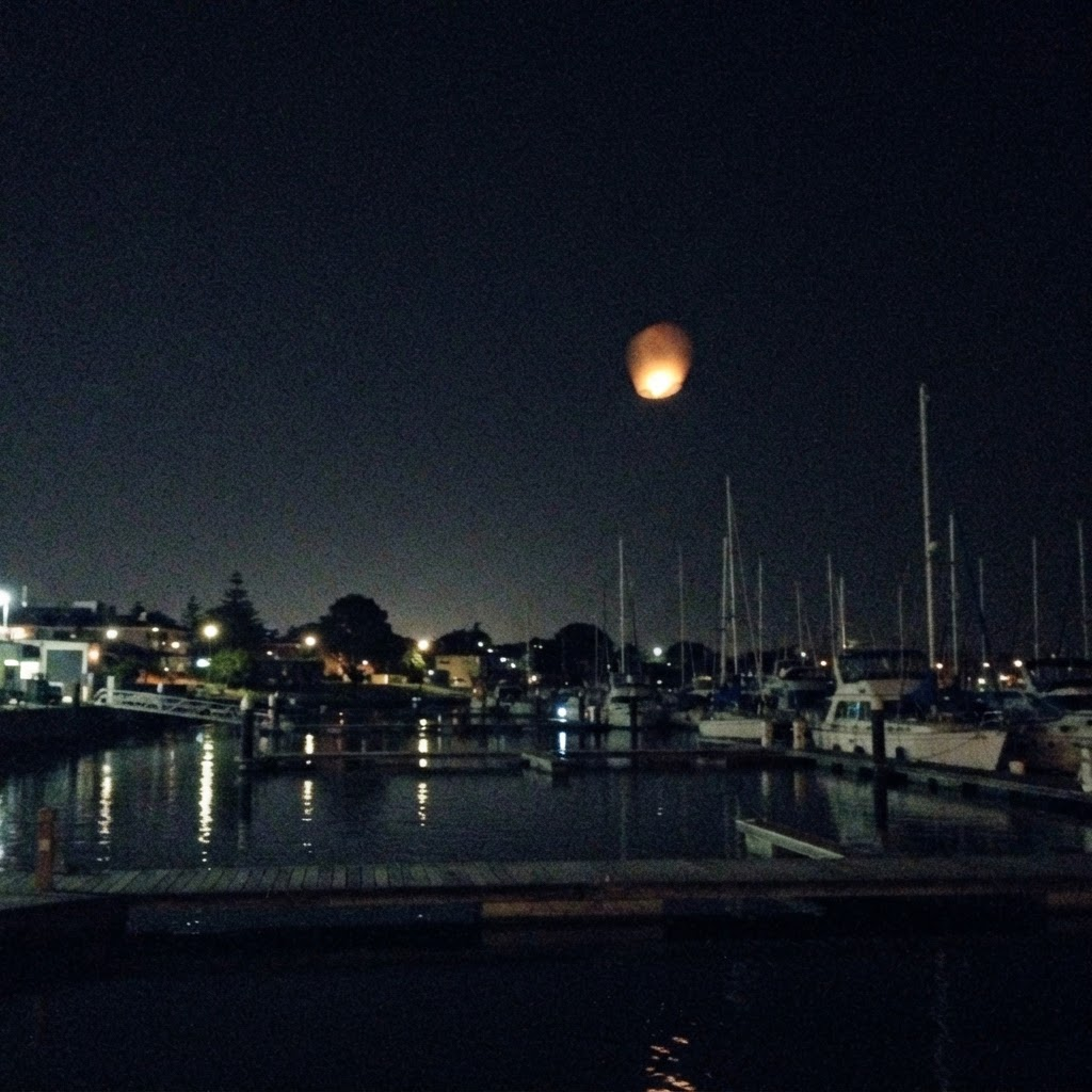Grainy night phone photo of a single amber light over a dim harbor marina.