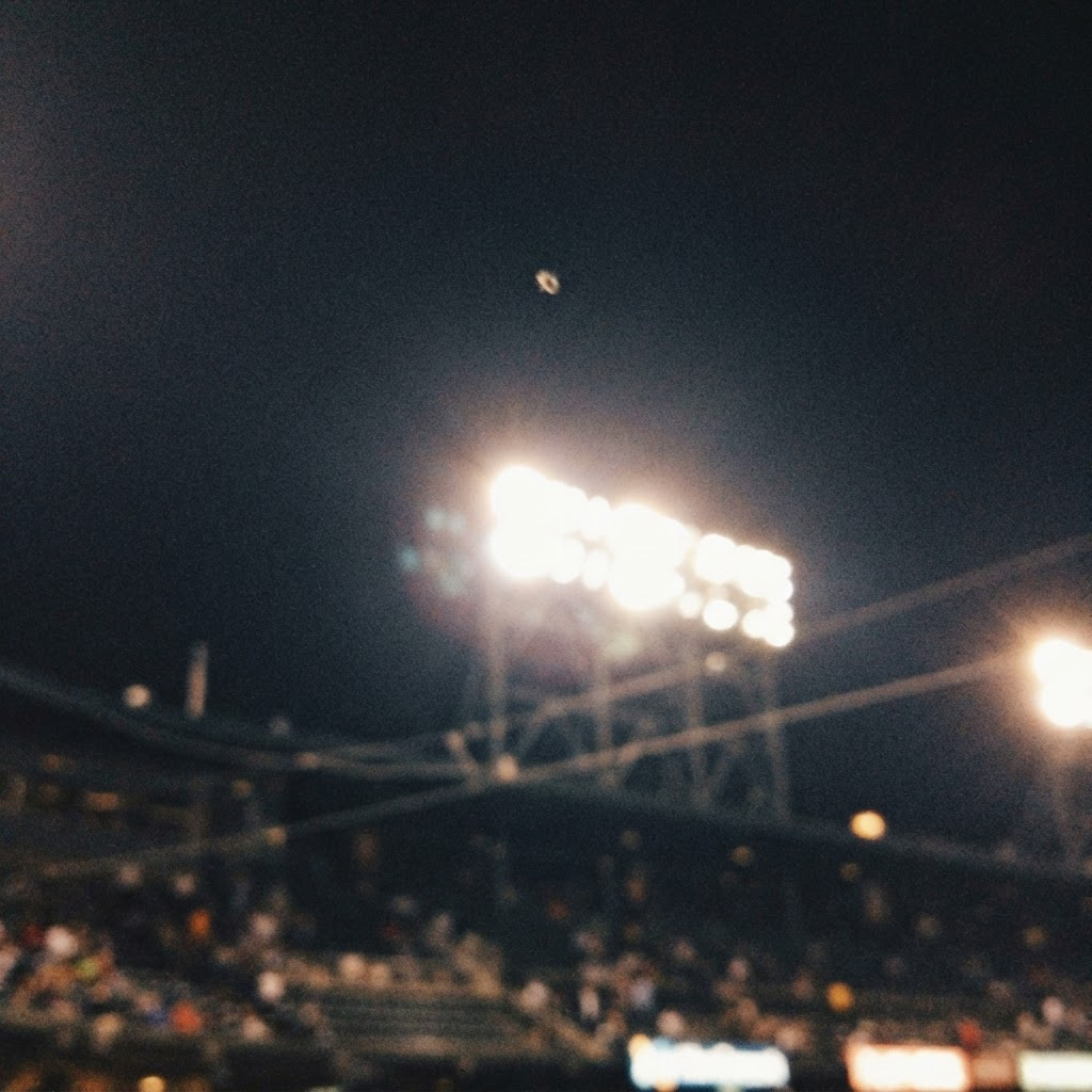 Very blurry phone photo of a tiny dot above bright stadium floodlights.